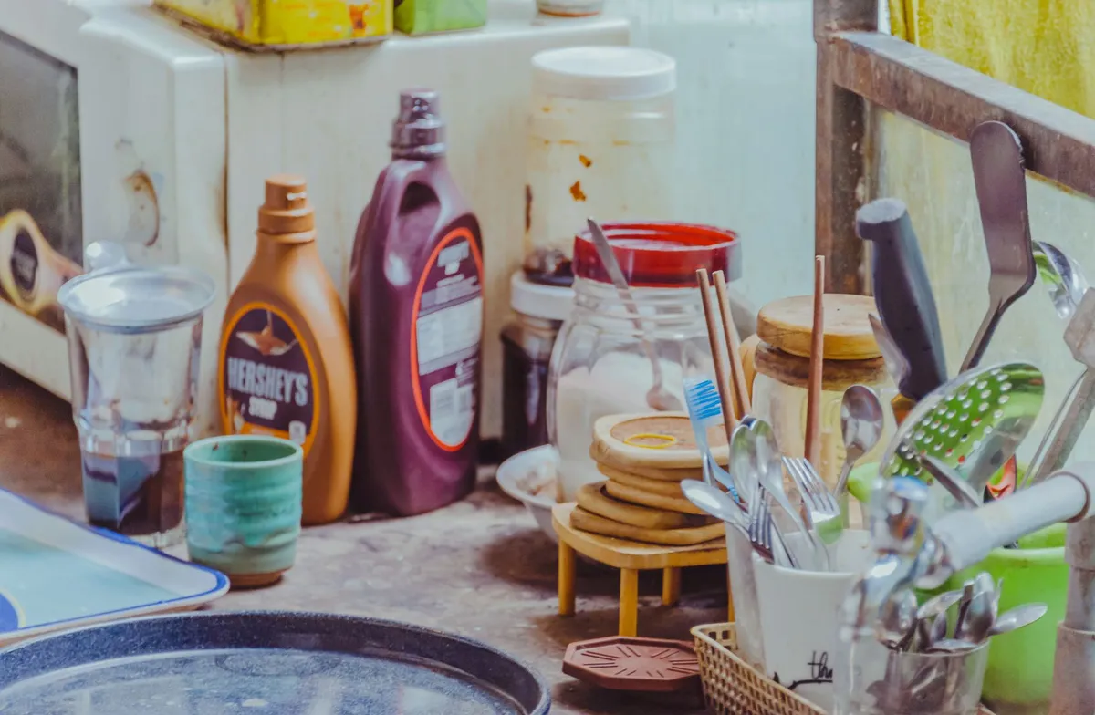 Counter with various household chemicals and utensils in a kitchen setting.
