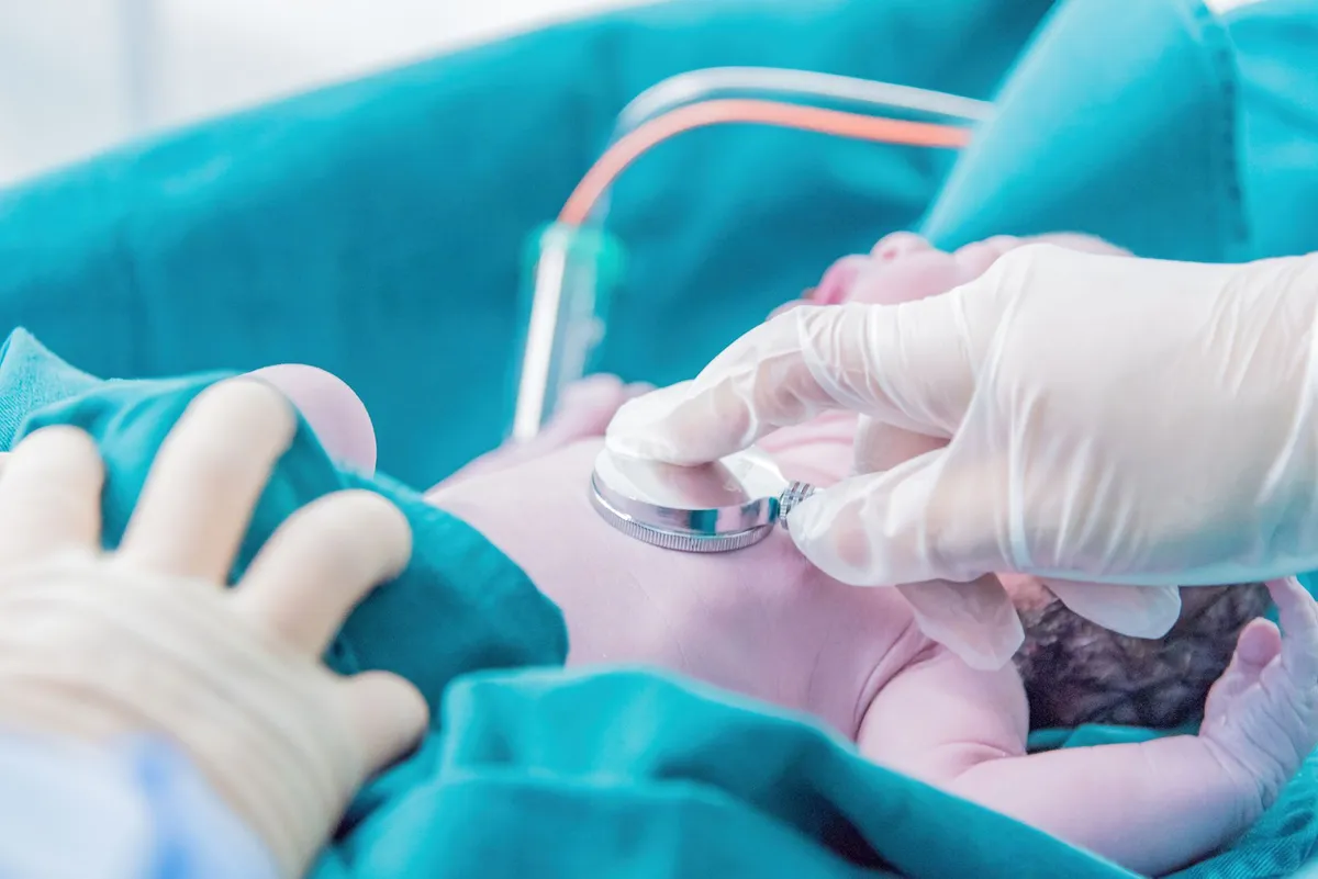 A healthcare professional using a stethoscope on a newborn baby.