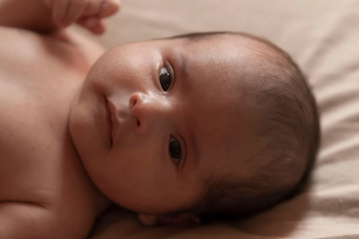 Newborn baby lying on a bed, looking directly at the camera.