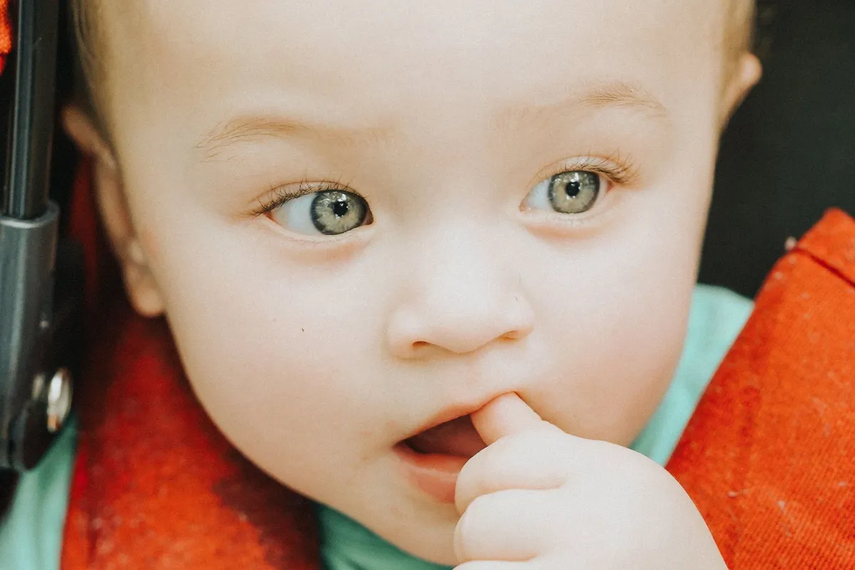 Close-up of a baby with blue eyes sucking on a finger, illustrating early development stages.