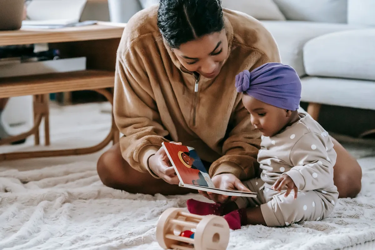 Parent reading a book to a six-month-old baby on a rug