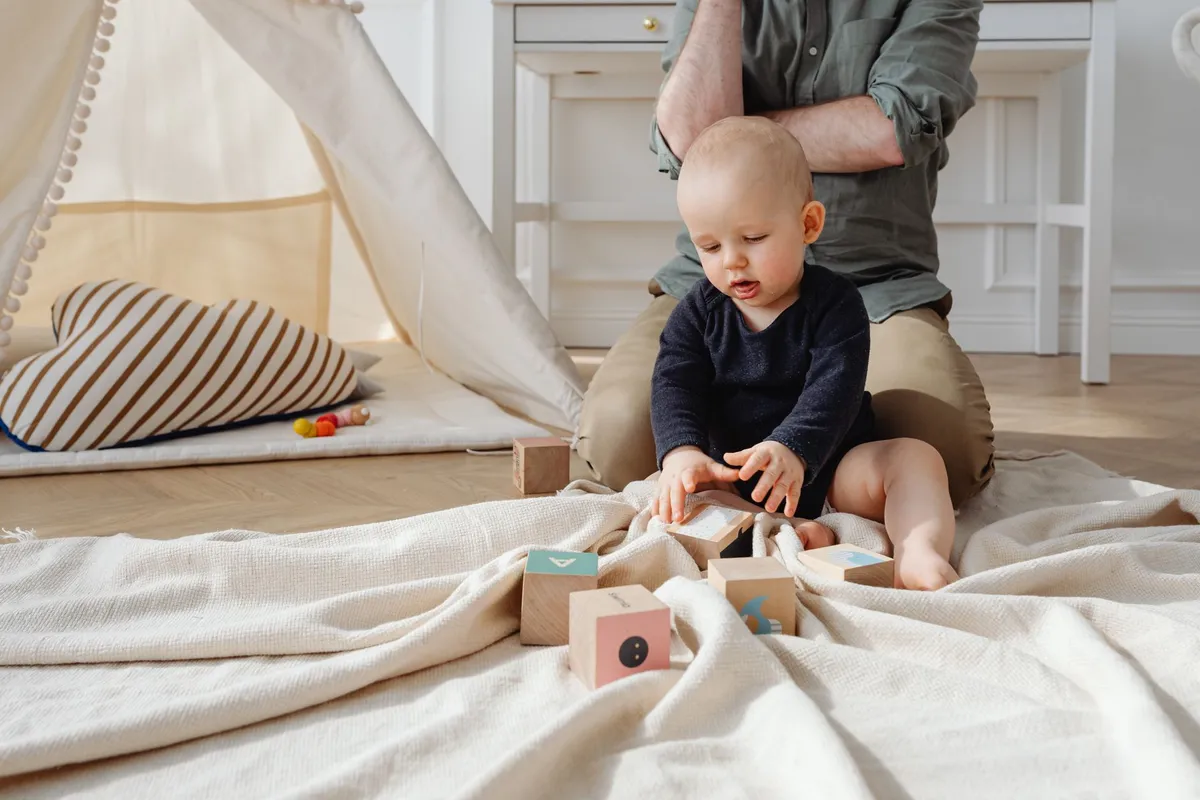 A baby playing with colorful blocks on a blanket, engaged with a caregiver nearby.