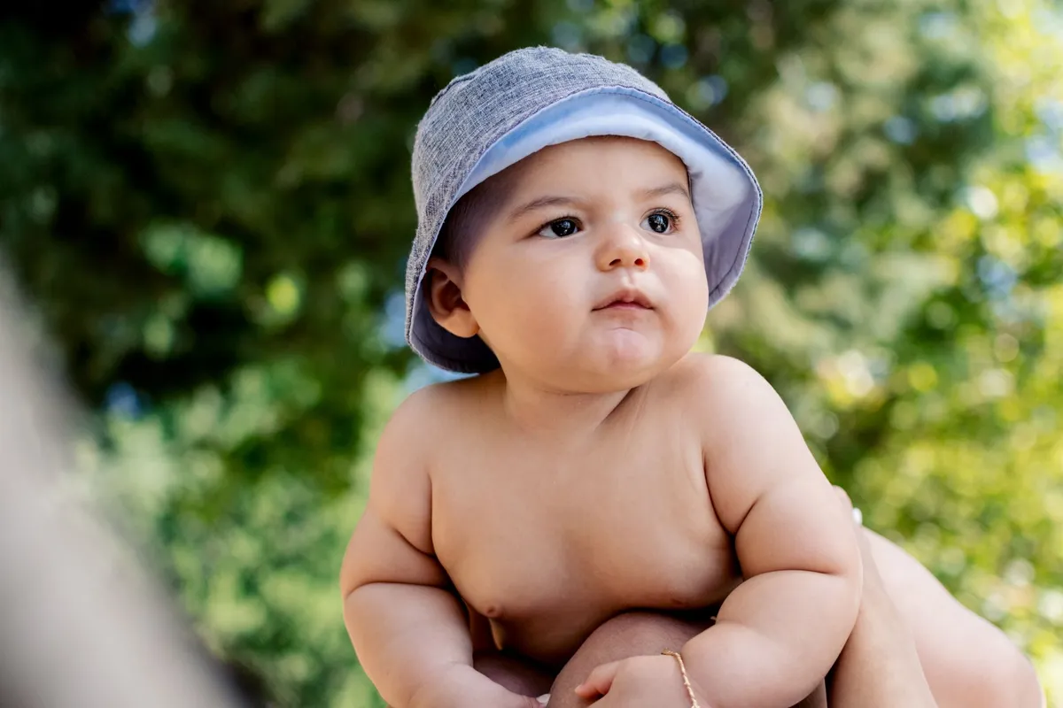 Baby with a hat looking thoughtfully outdoors, illustrating early motor development.