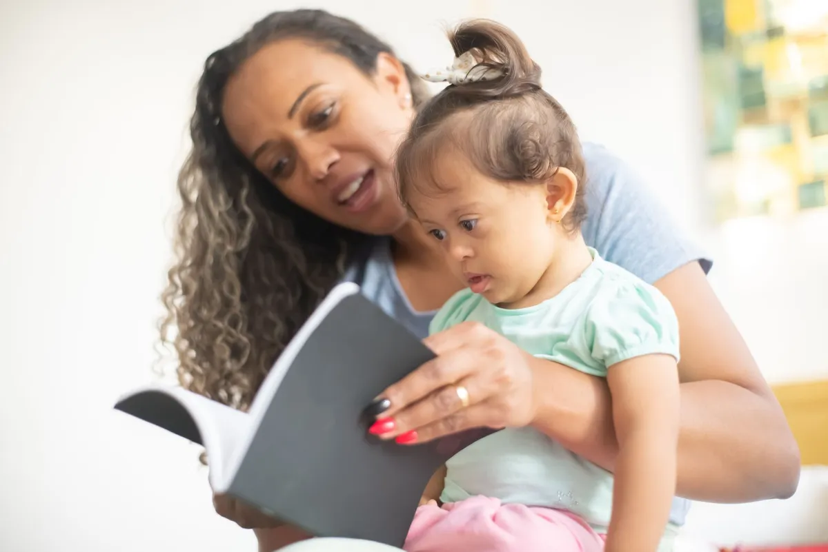 Parent reading to a toddler, both engaged with a book in a bright room.