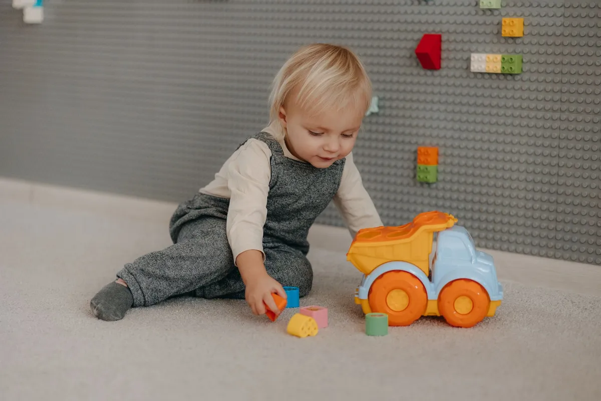 Toddler playing with colorful building blocks and a toy truck on a soft surface.
