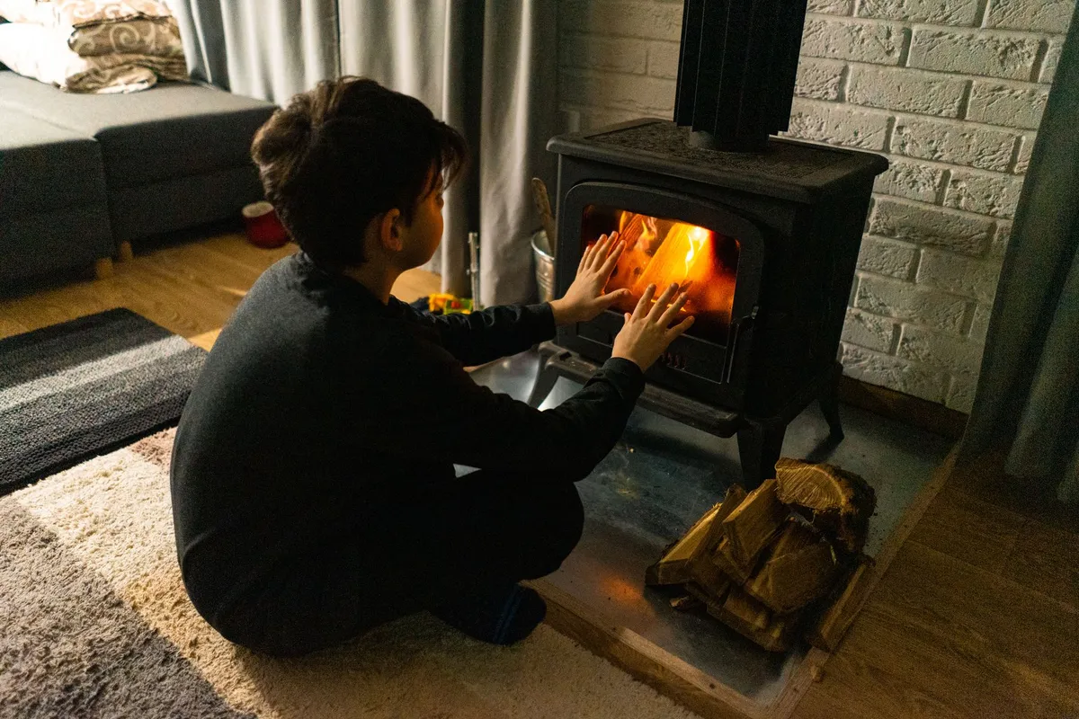 Child warming hands by a wood stove in a cozy home setting.