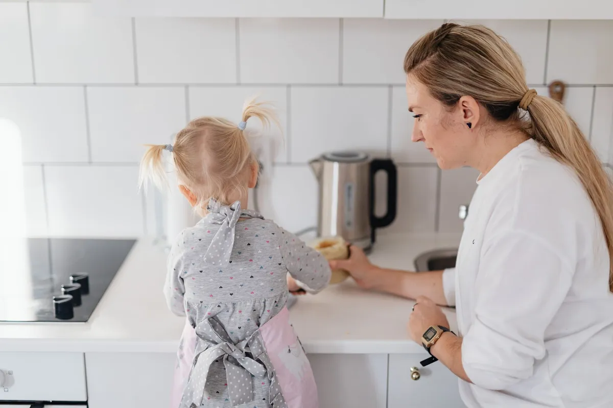Child in an apron helping an adult in the kitchen.
