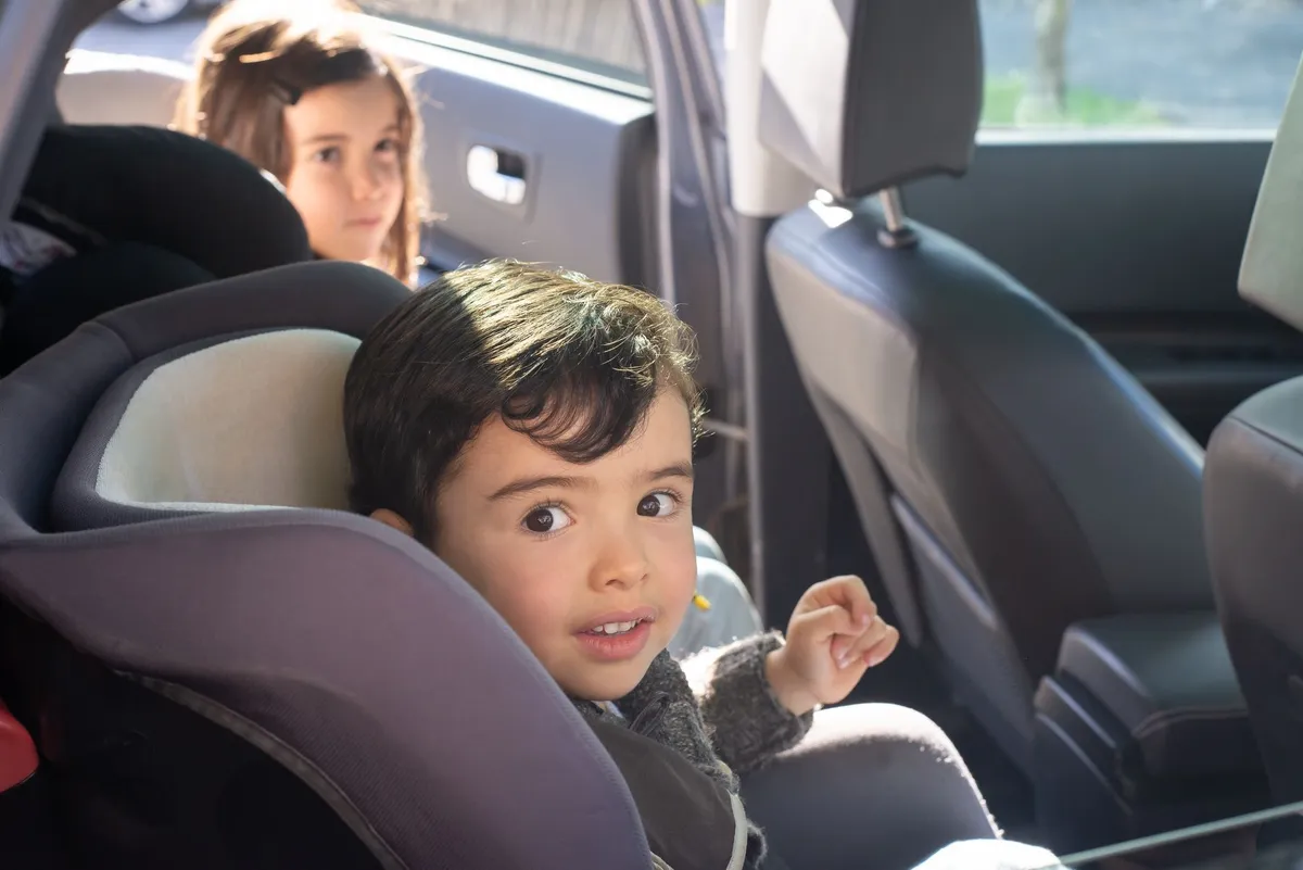 Two children in car seats, one looking at the camera, the other in the background.