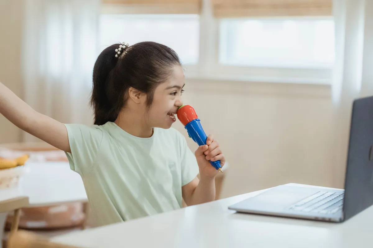 Child singing into a microphone while looking at a laptop screen.