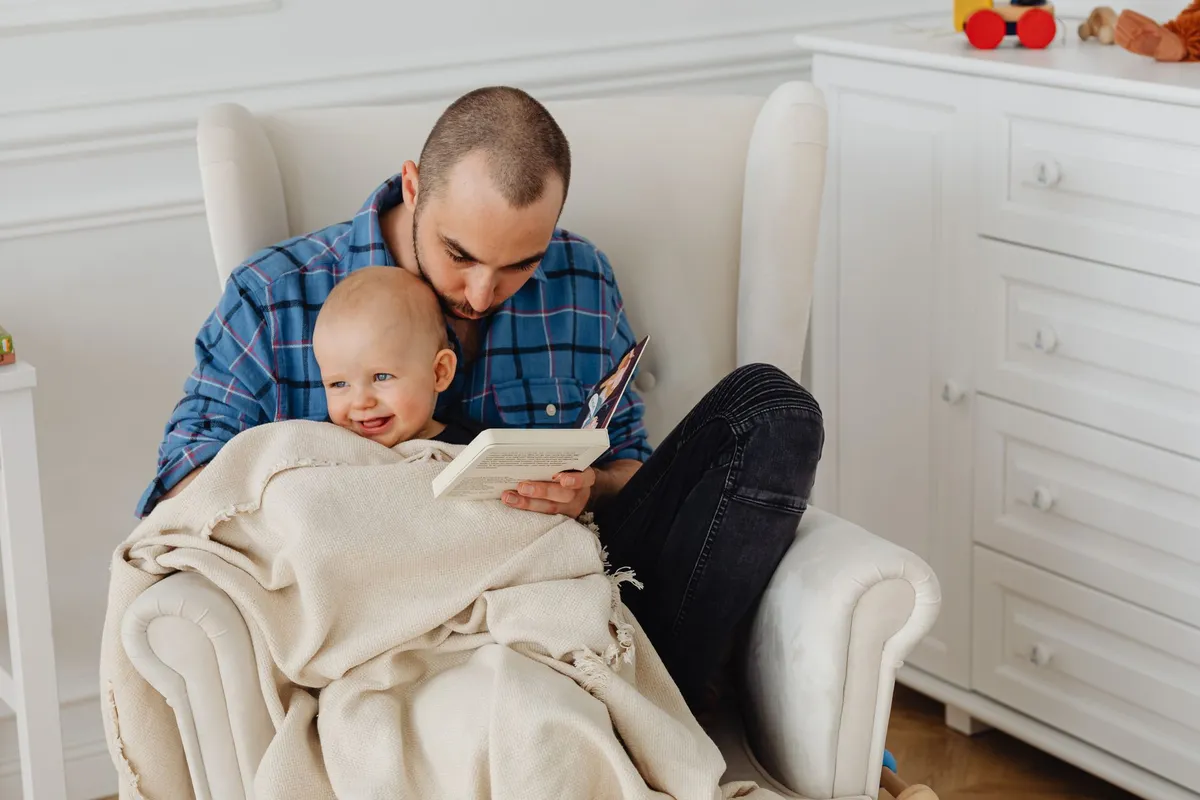 A parent reading to a baby in a cozy chair, wrapped in a blanket.