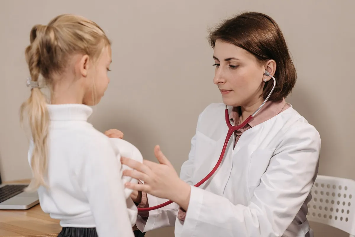 Pediatrician examining a child with a stethoscope in a clinical setting.