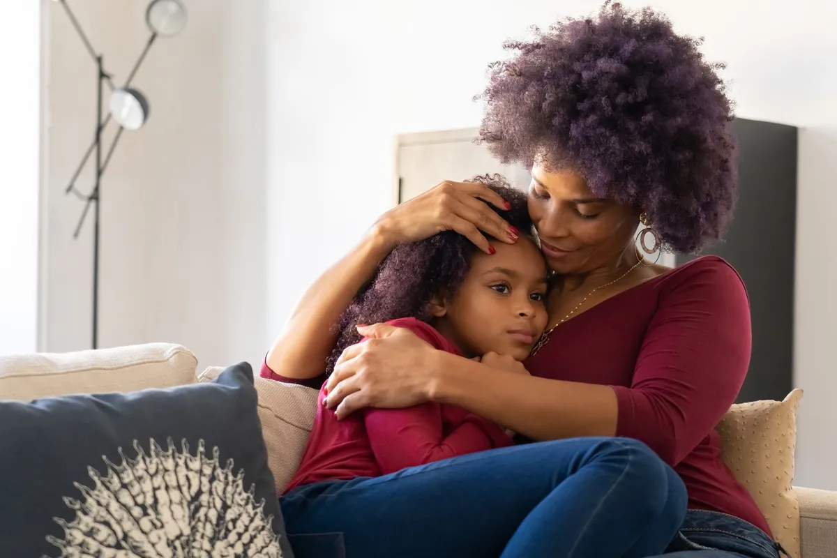 A mother comforting her shy daughter on a couch, showing a nurturing moment.