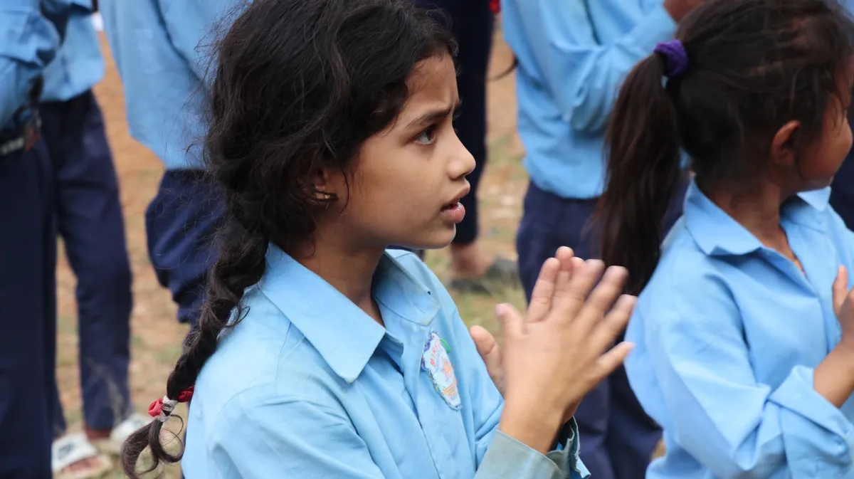 A shy girl with clasped hands, looking anxious in a group setting.