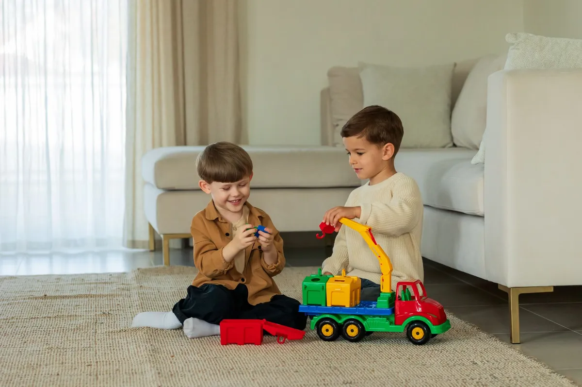 Two boys playing with toy trucks on a rug in a living room.