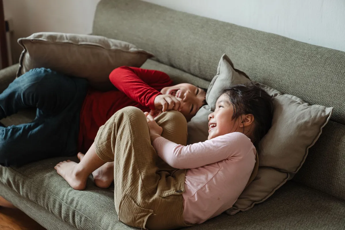 Two children laughing and playing together on a couch, illustrating sibling interaction.