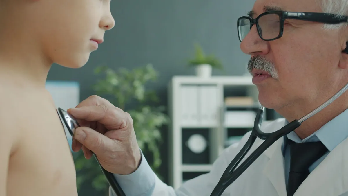 Pediatrician examining a child’s chest with a stethoscope in a clinical setting.