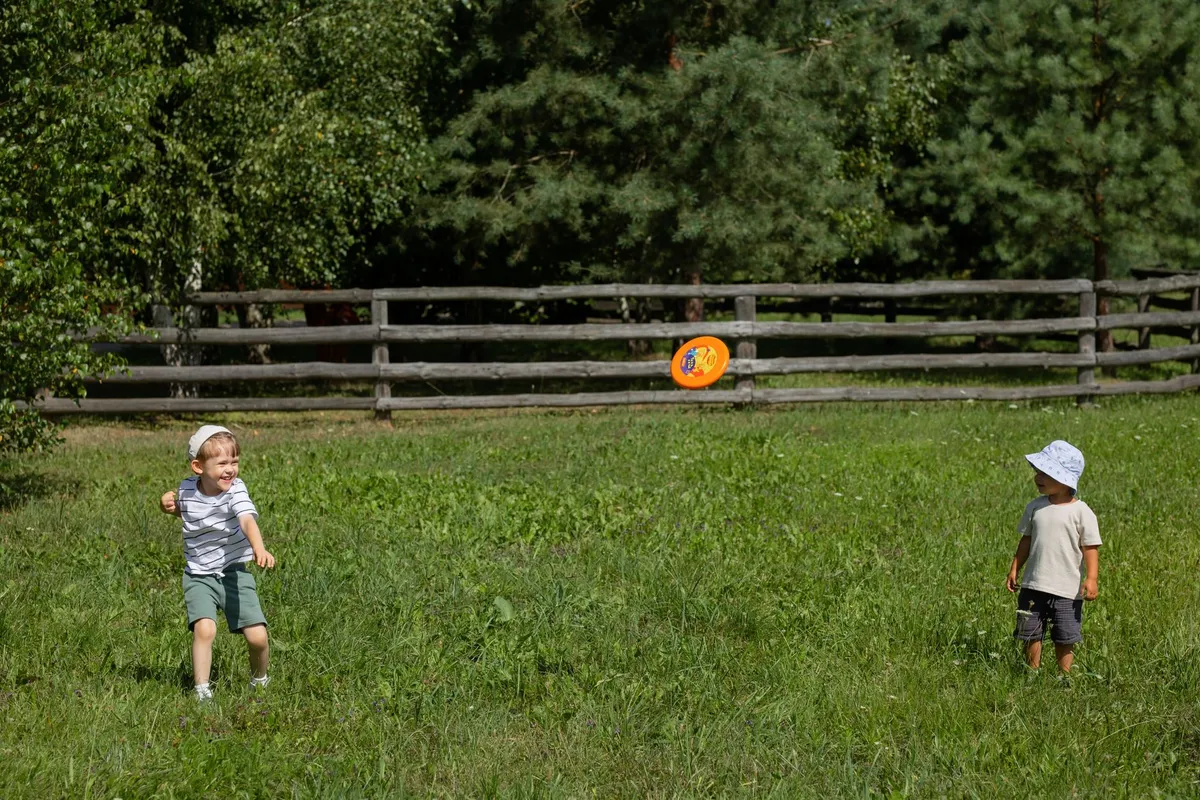 Two children playing frisbee in a grassy field with a wooden fence in the background.