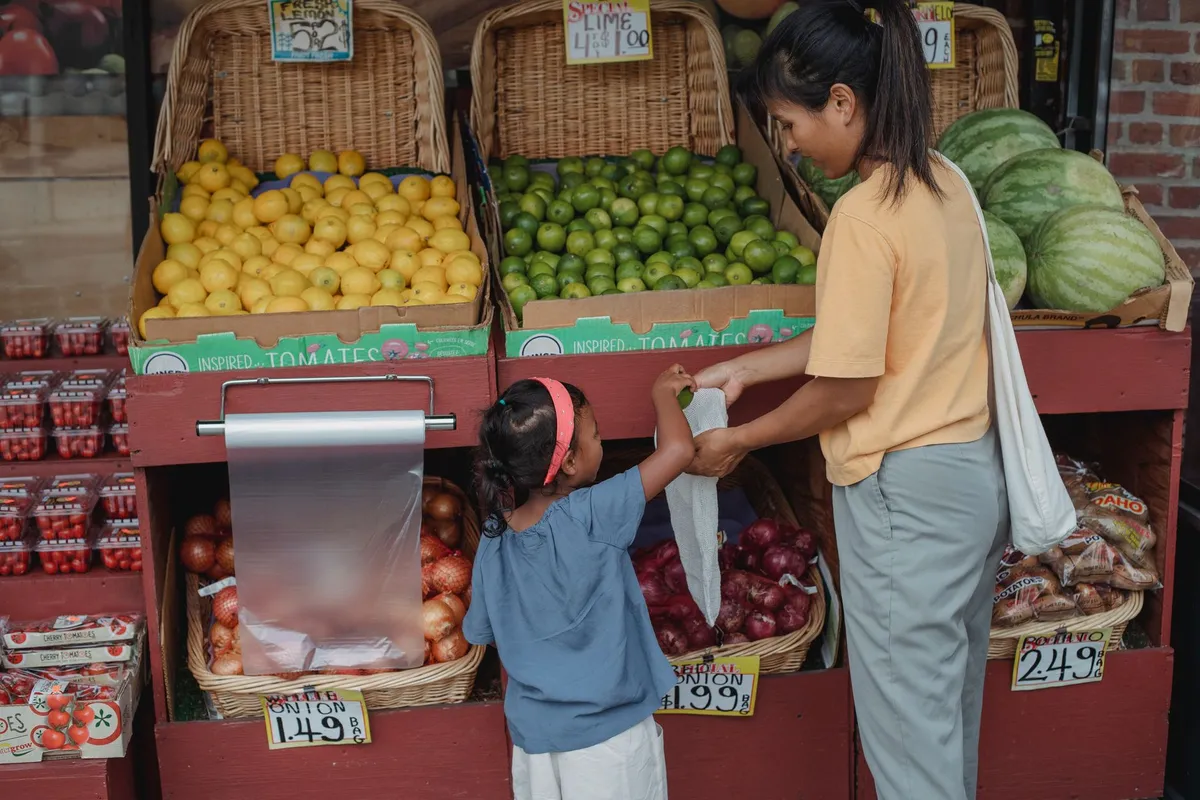 A mother and child selecting fresh fruits and vegetables at a market stand.