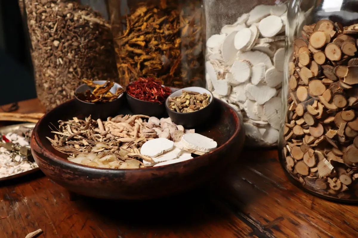 Various Chinese herbs in bowls on a wooden table with jars in the background.