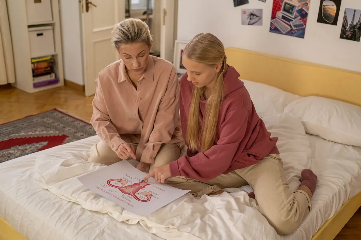 Two women examining a diagram of the female reproductive system on a bed.