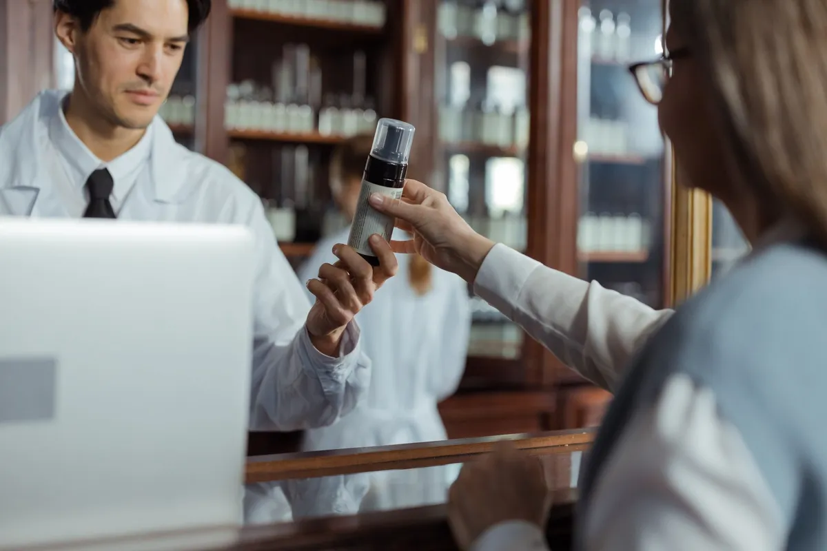 Pharmacist handing a customer a medication bottle at a pharmacy counter.