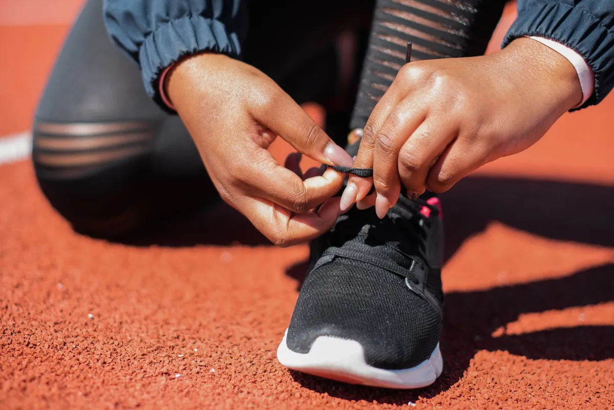 Person tying shoelaces on a black athletic shoe on a running track.