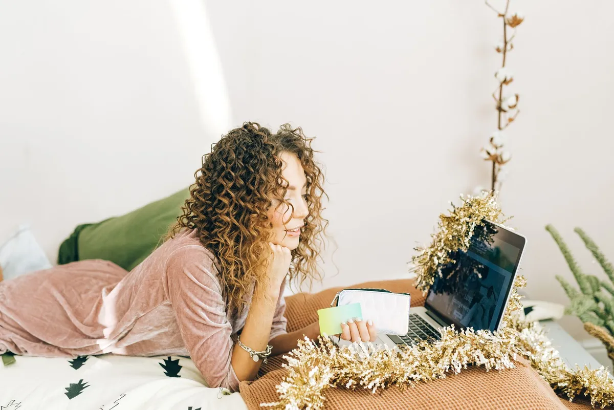 Person budgeting for Christmas shopping with notes and a laptop.