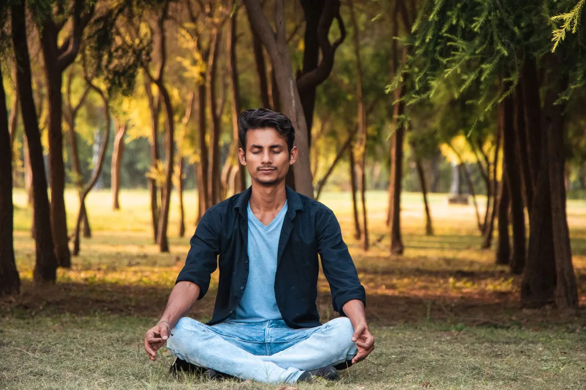 Man meditating in a park surrounded by trees, promoting mindfulness and stress relief.