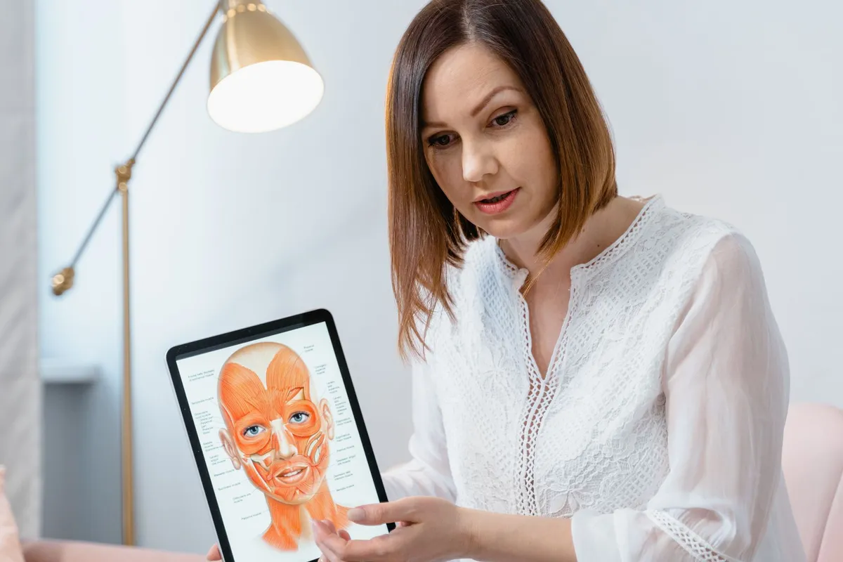 Woman showing a digital tablet with a facial muscle diagram, relevant to cleft lip anatomy.
