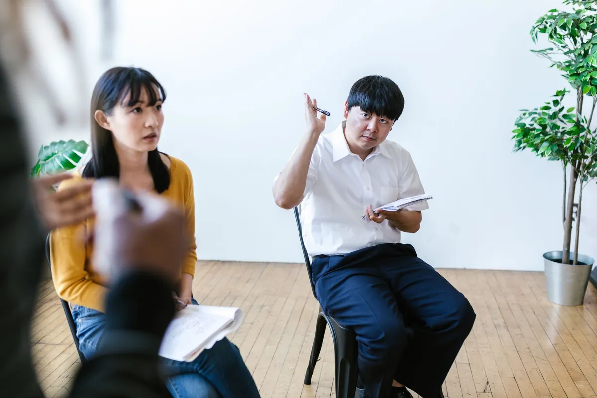Two participants in a therapy session, one speaking and one listening attentively.