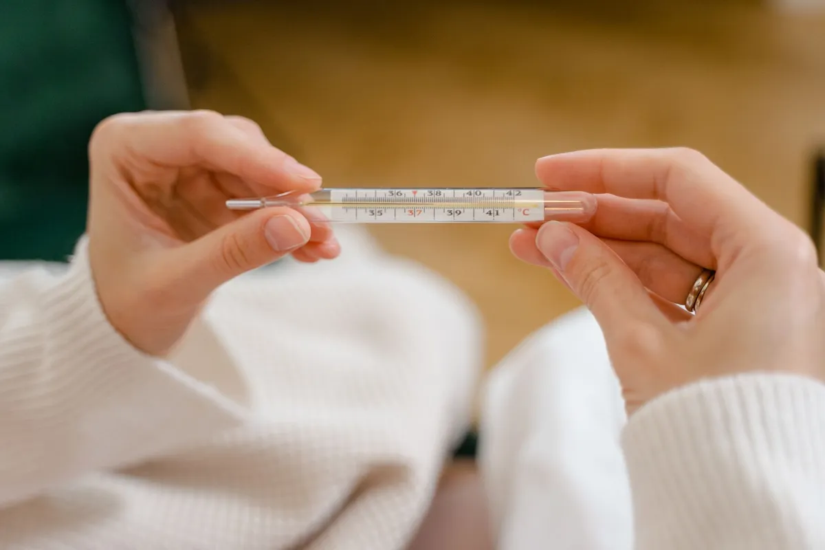 Person holding a thermometer showing a temperature reading.