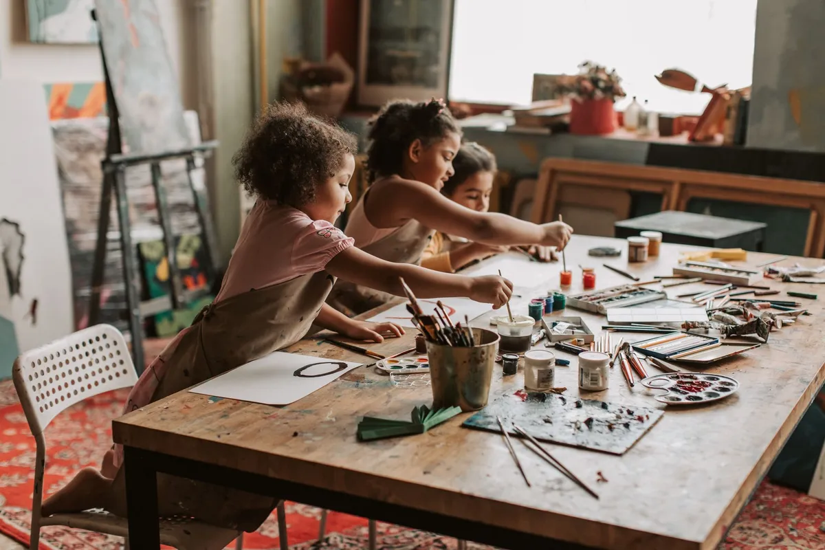 Three children painting with various colors at a table in an art studio.