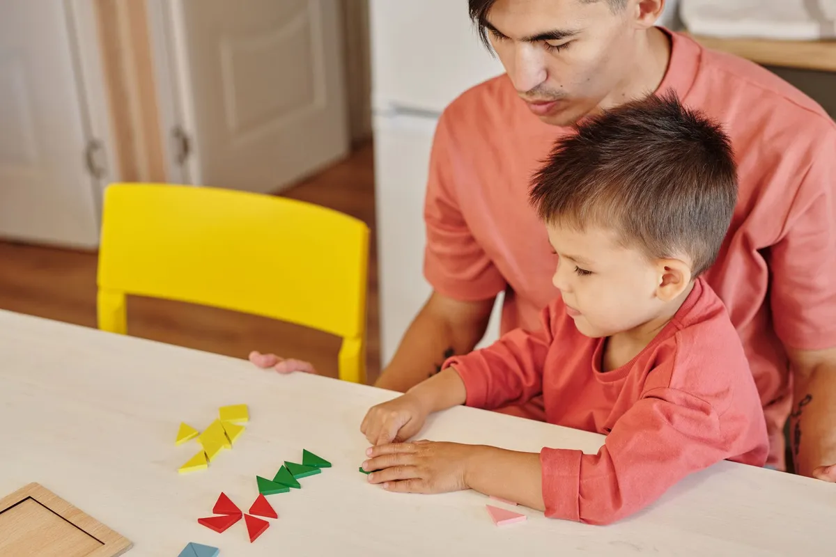A parent and child engaged in a creative activity at a table with colorful shapes.