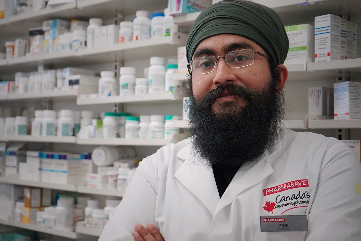 Pharmacist in a pharmacy with shelves of medications in the background.