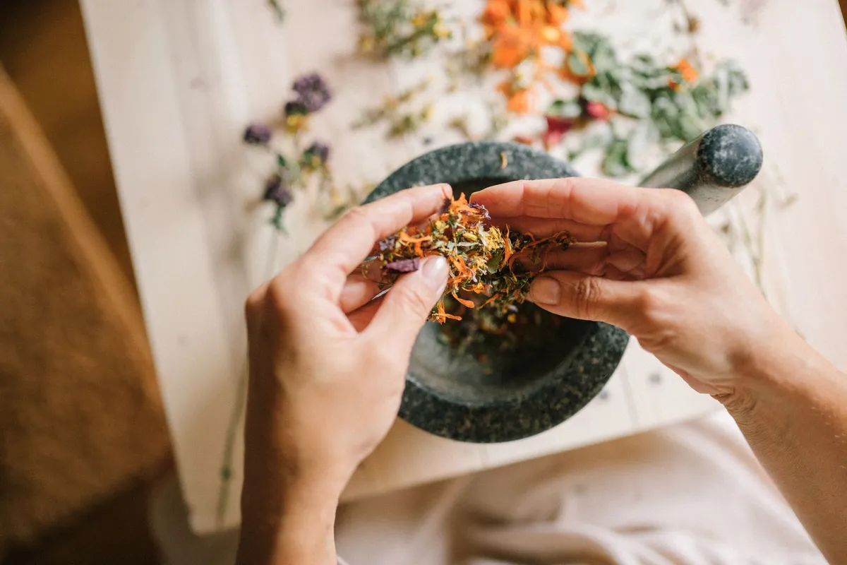 Hands mixing dried herbs in a mortar and pestle on a wooden table.