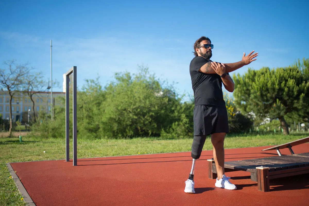 Man with a prosthetic leg stretching his arm in a park setting.