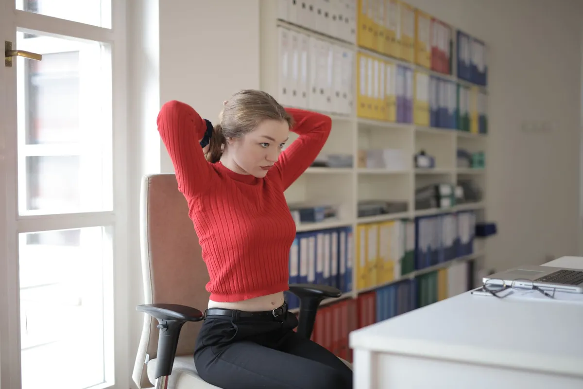Woman sitting at a desk, stretching her arms behind her head in an office setting.