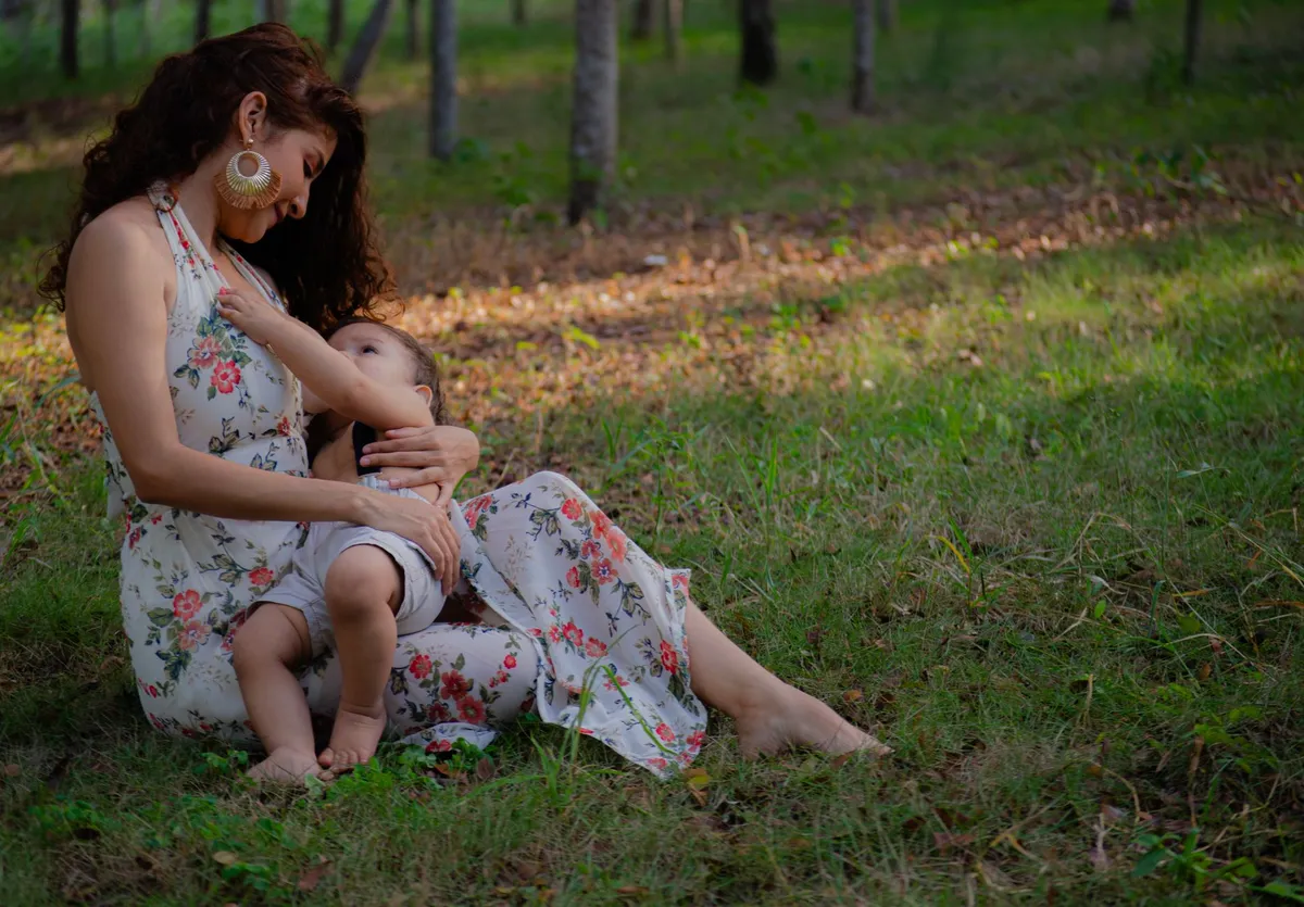 Mother breastfeeding her child while sitting on the grass in a natural setting.