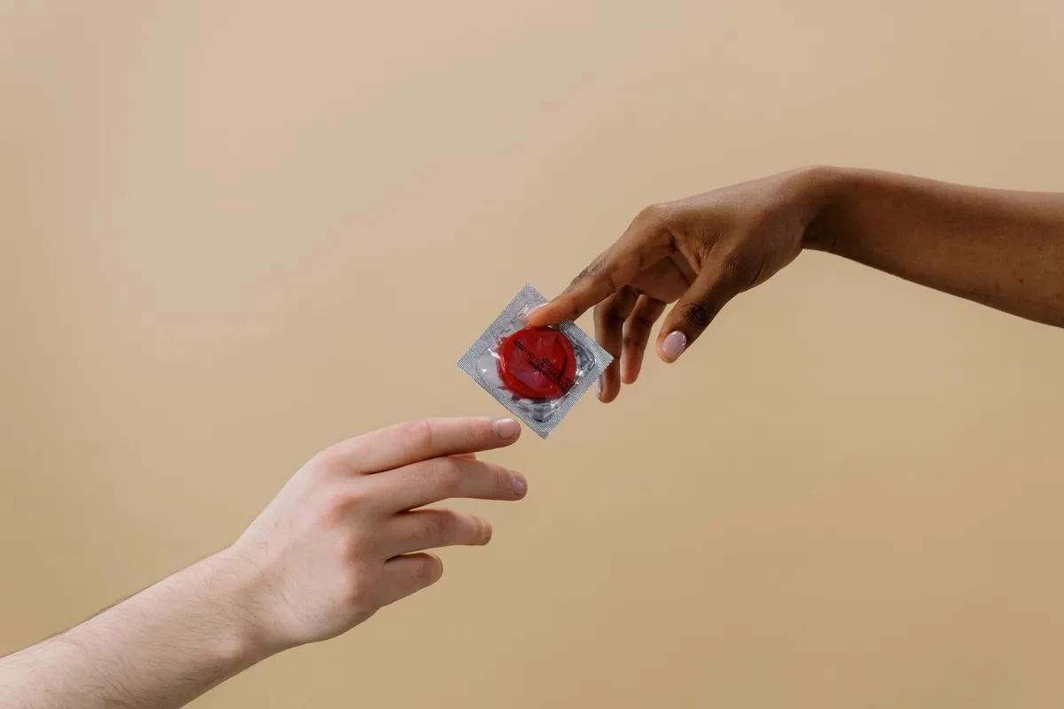 Hands exchanging a condom package, representing contraception options.