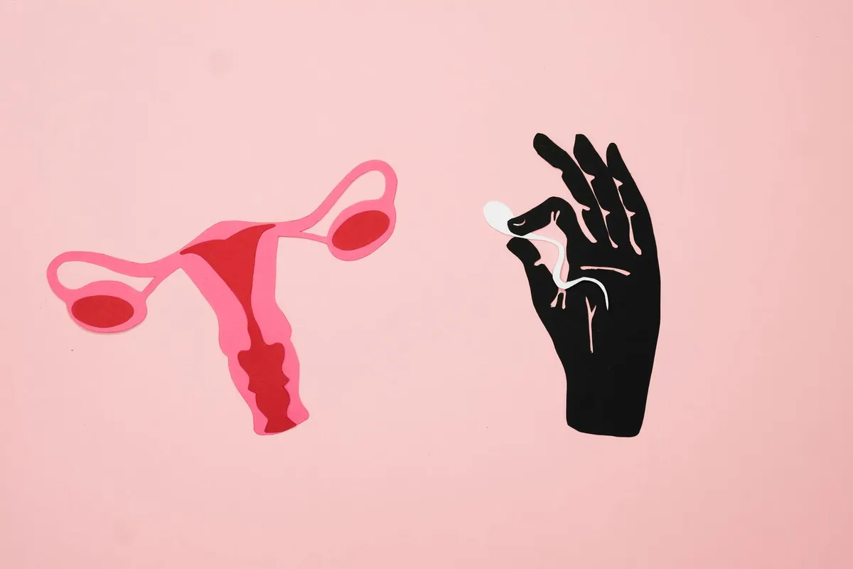 Illustration of uterus and hand holding a contraceptive pill on a pink background.