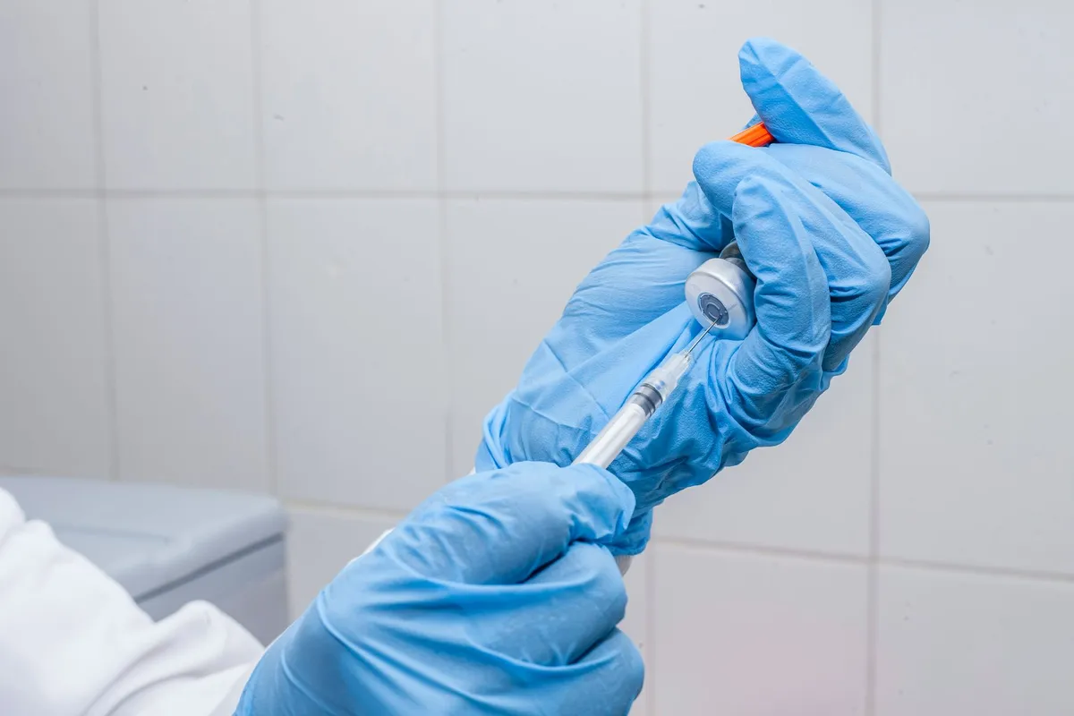 A gloved hand preparing a syringe with a vial for injection.