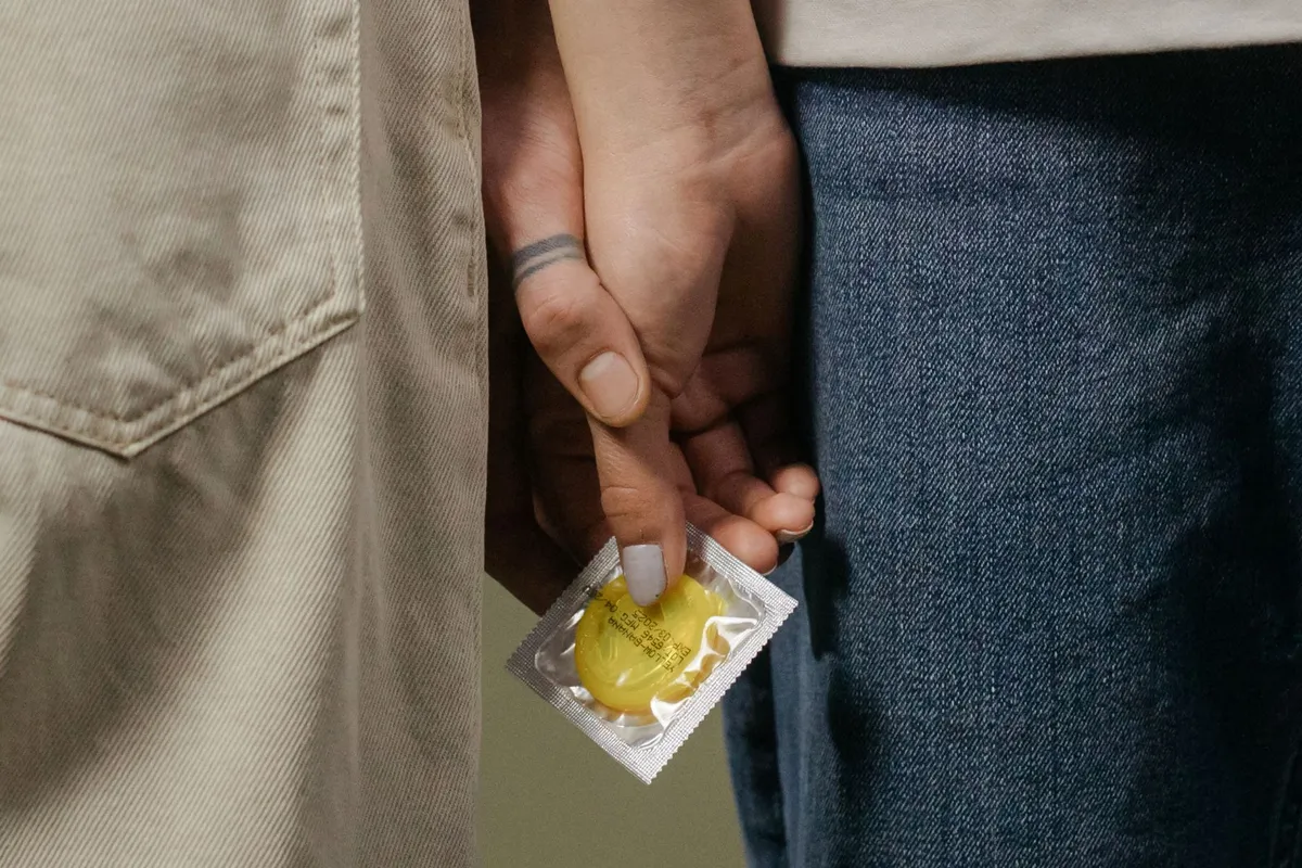 Couple holding hands with a condom package visible between them.