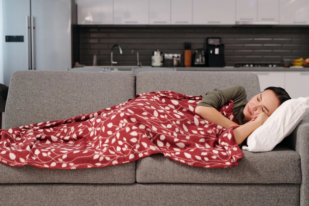 Person resting under a blanket on a couch, illustrating convalescence.