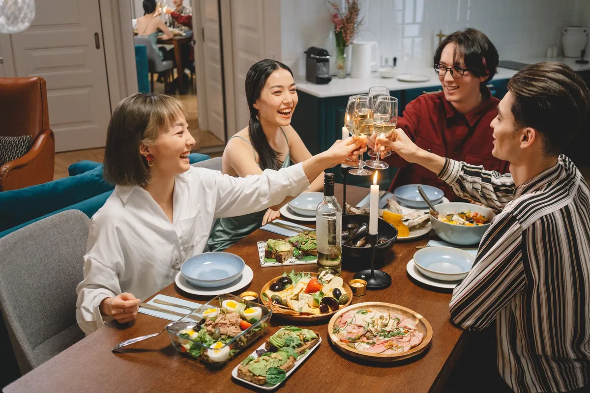 Group of friends toasting with drinks at a dinner table with various dishes.