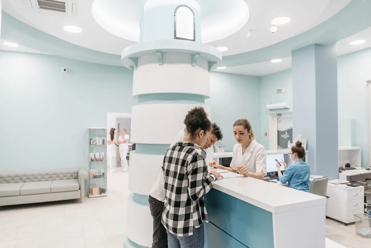 Patients at a hospital reception area interacting with staff at a desk.