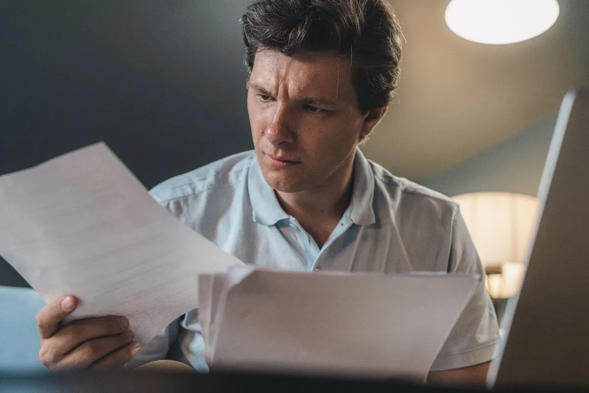 Man reviewing medical documents at home with focused expression.