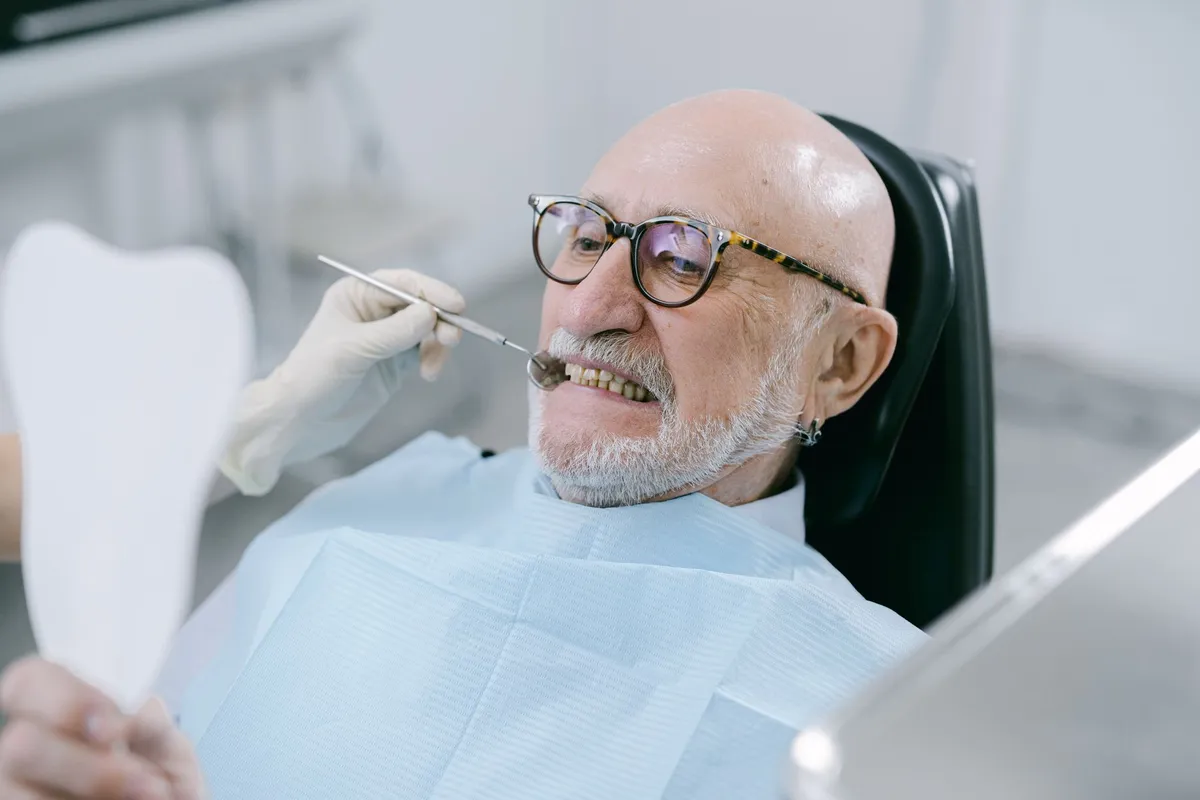 Older man in dental chair smiling while looking at his reflection.