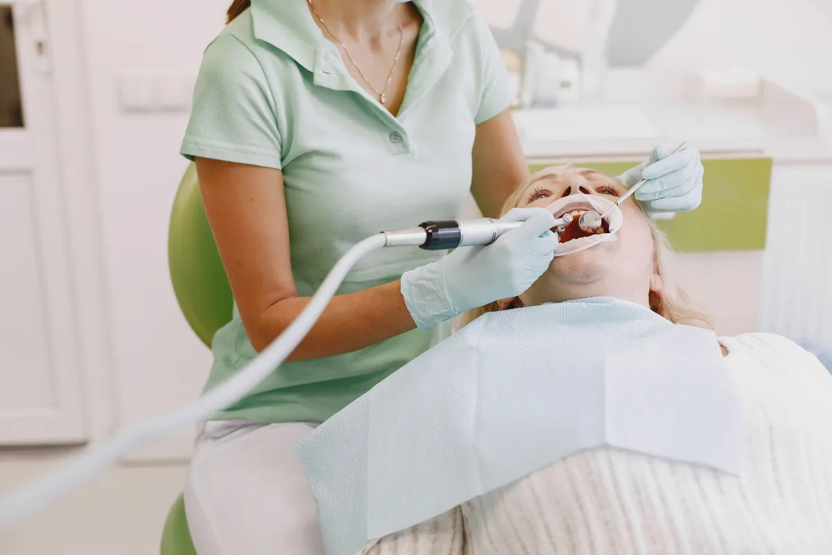 Dental hygienist cleaning a patient’s teeth in a clinical setting.