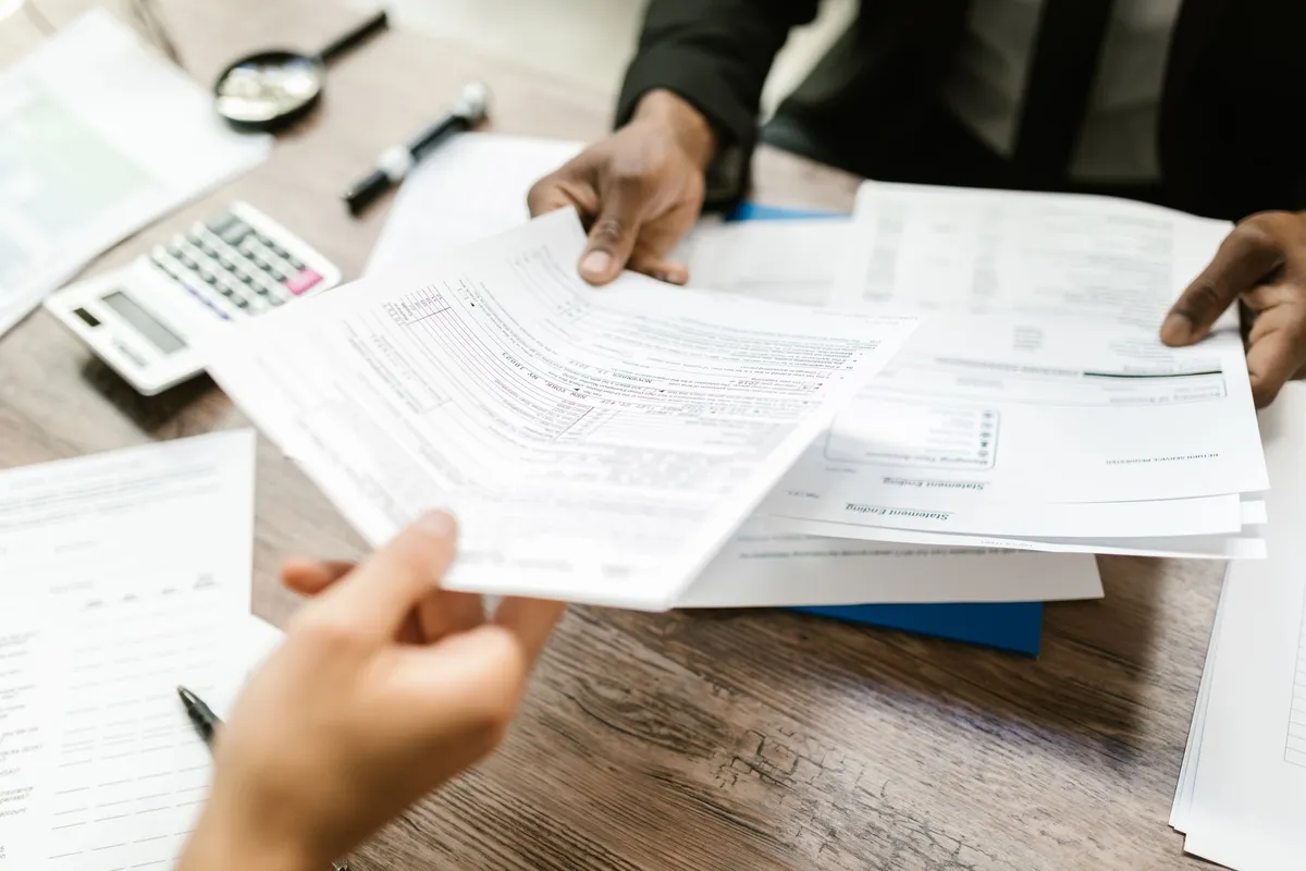 Hands exchanging documents with insurance forms on a table.