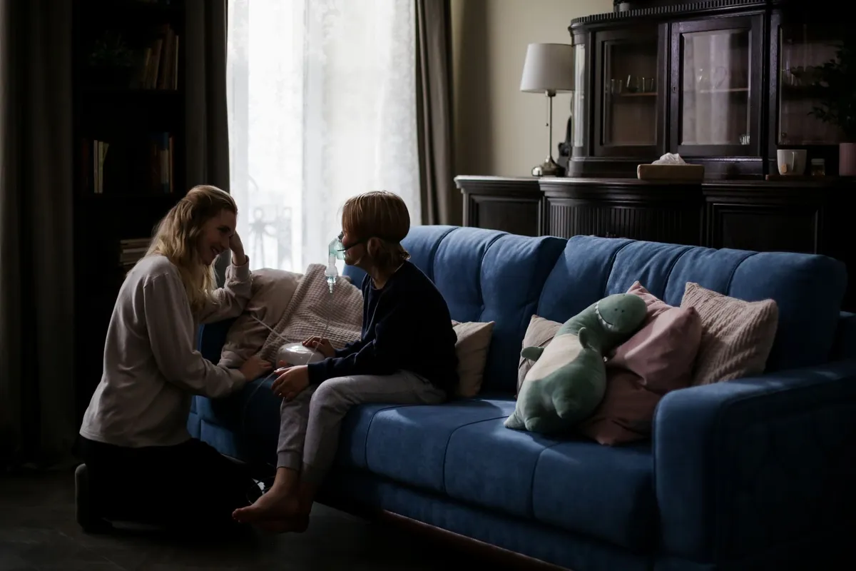 Child sitting on a couch with a caregiver, both appearing concerned in a living room setting.
